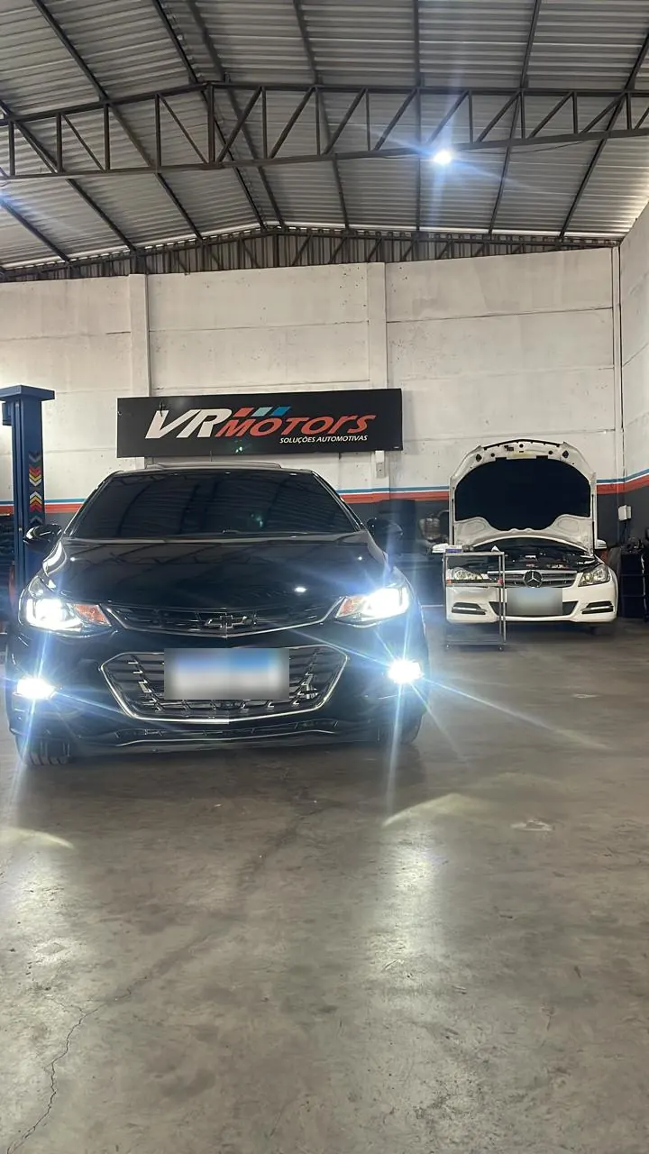 Carro com faróis acesos dentro da oficina VR Motors, sob o letreiro da empresa